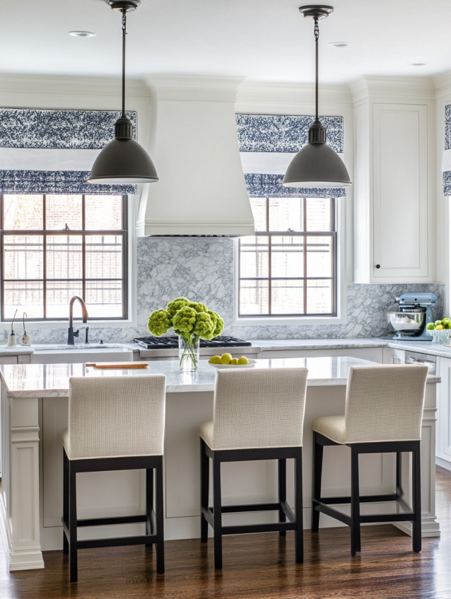 White kitchen with marble backsplash and countertops, large grey pendant lights, Roman shades and upholstered stools.