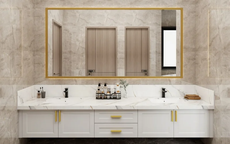 Modern double-sink vanity with a marble countertop, white cabinetry, and gold accents, complemented by a large gold-framed mirror.